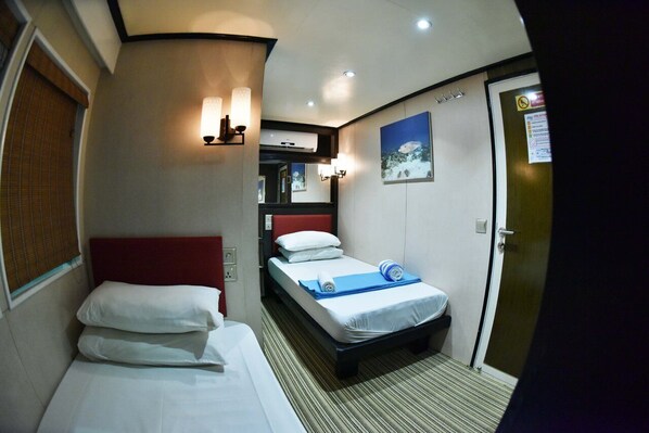 A hotel room with two beds, a red headboard, a wall-mounted air conditioner, a painting, and a door with a sign.