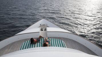 Cubierta de barco con dos personas acostadas sobre una alfombra a rayas, mirando al océano.