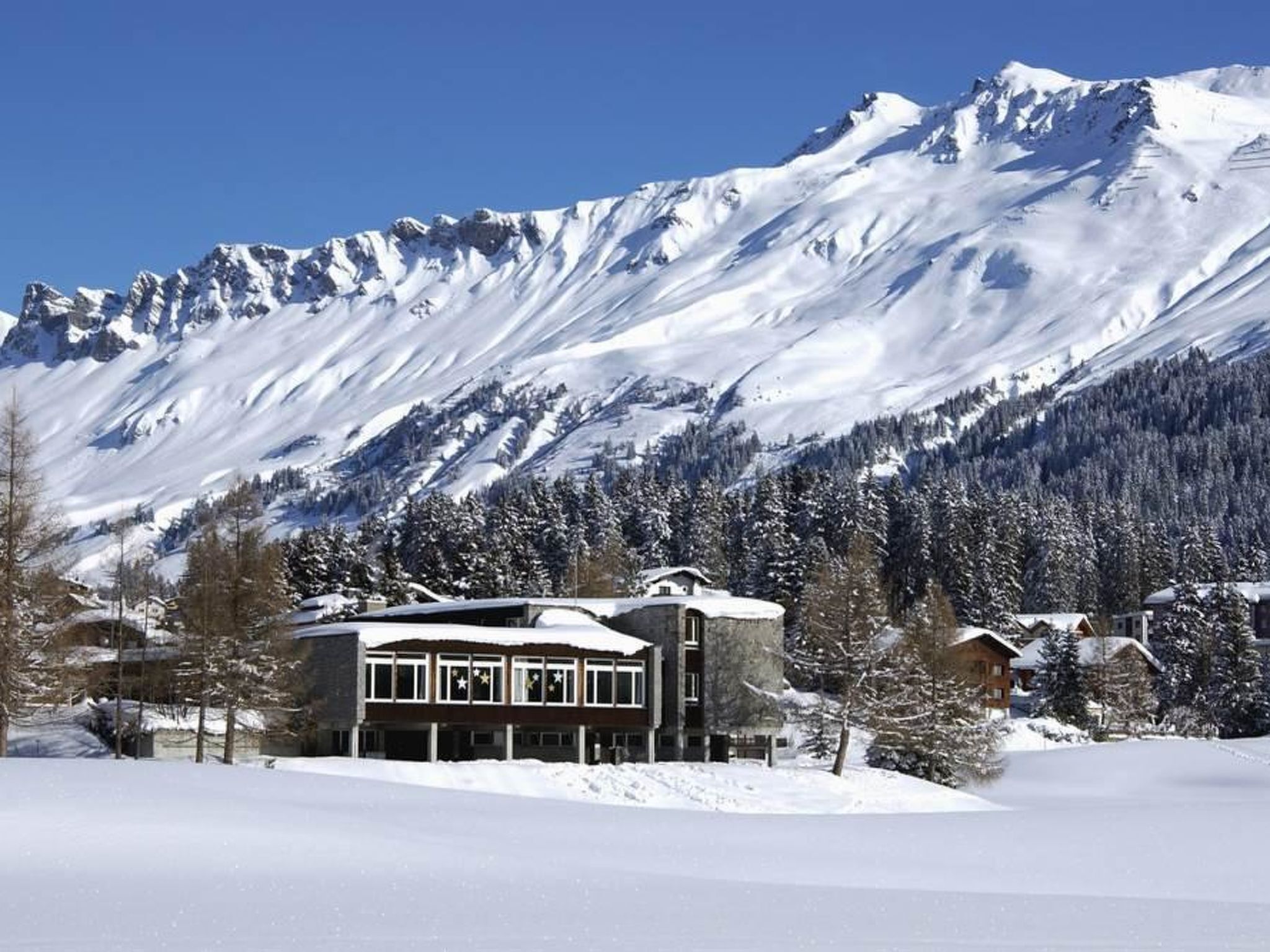 Ein mit Schnee bedeckter Berg mit einem Gebäude, das große Fenster und eine Steinfassade hat.