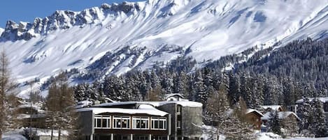 A snow-covered mountain with a building featuring large windows and a stone facade.
