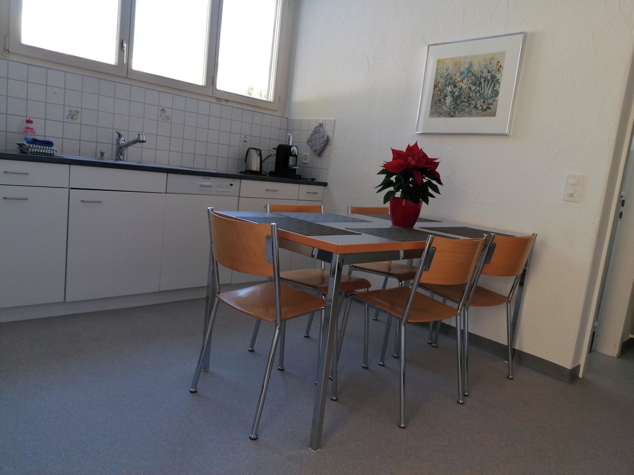 Een keuken met een eettafel, stoelen, een potplant en een raam.