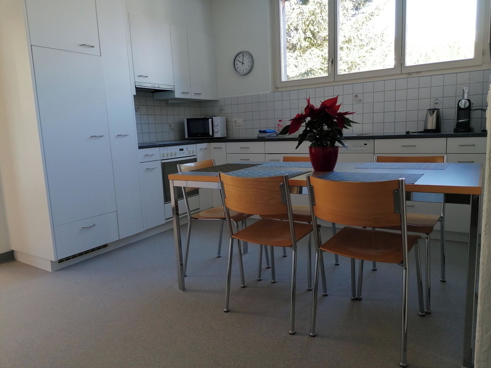 A kitchen with white cabinets, a microwave, a clock, and a dining area with a table and chairs.