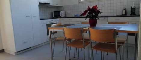 A kitchen with white cabinets, a microwave, a clock, and a dining area with a table and chairs.