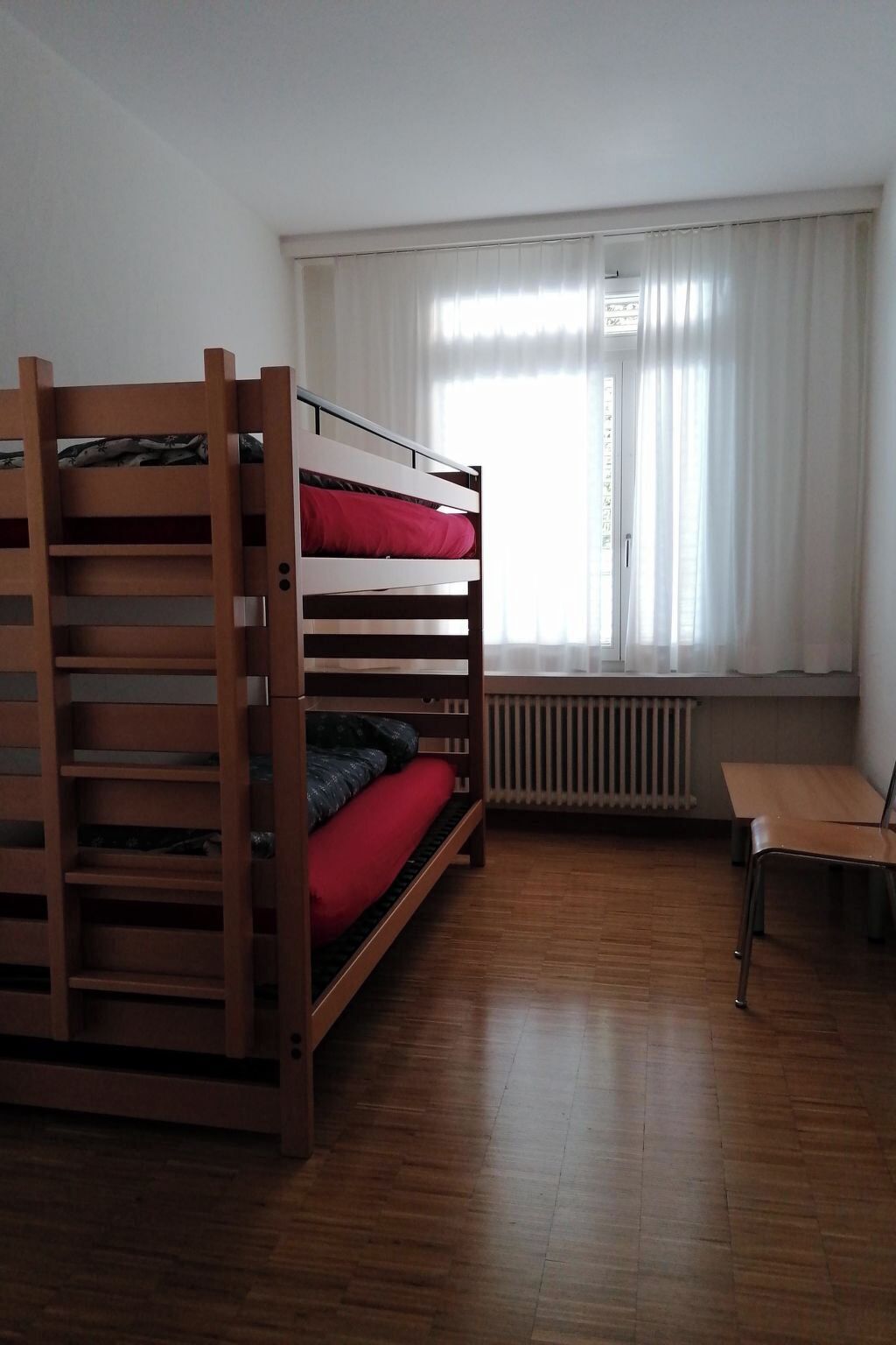 Une chambre avec un lit superposé, une table et un radiateur.