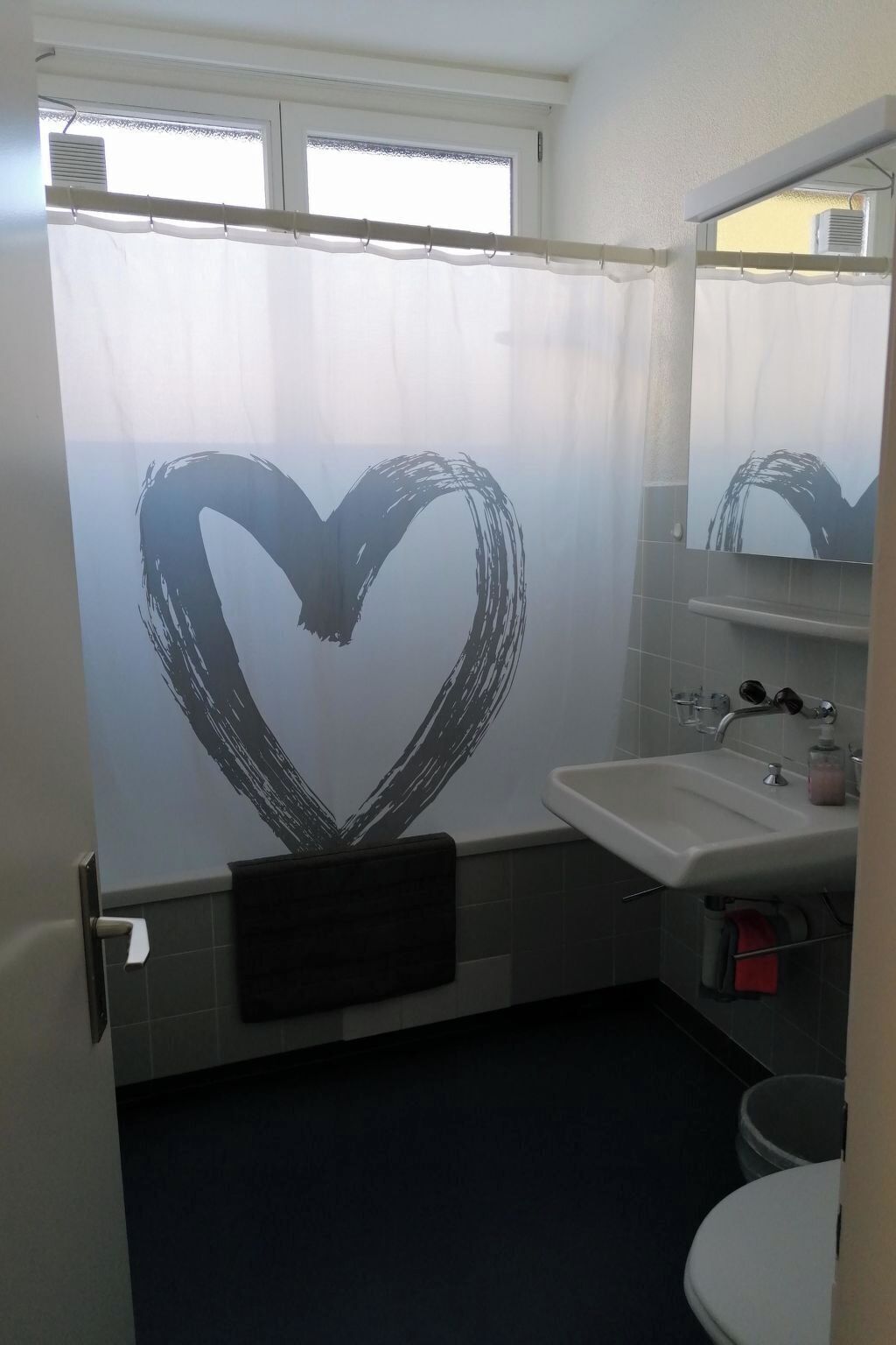 Een badkamer met een hartvormig ontwerp op het douchegordijn, een wastafel en een toilet.