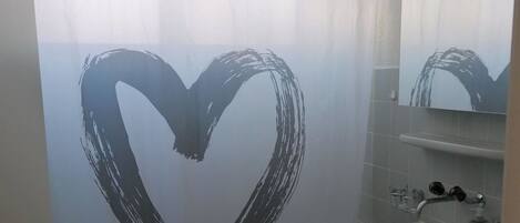 Een badkamer met een hartvormig ontwerp op het douchegordijn, een wastafel en een toilet.