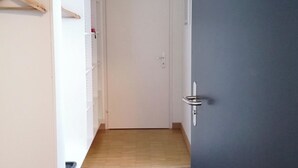 Un pasillo con una puerta que da a una habitación, un perchero y una lámpara en el techo.