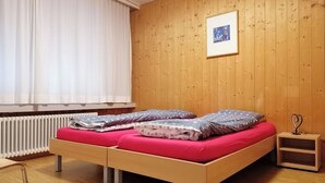Una habitación con suelo de madera, una cama con dos almohadas, una mesita de noche y un radiador.