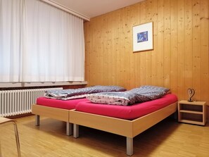 Ein Zimmer mit Holzboden, einem Bett mit zwei Kissen, einem Nachttisch und einer Heizung.