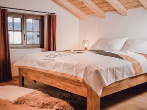 Un dormitorio con cama de madera, una ventana con cortinas, una mesita de noche con lámpara y vistas al exterior.