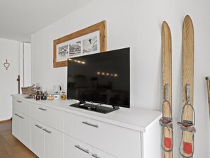 A modern living room with a flat-screen TV, a framed photo collage, and skis leaning against the wall. - Nr.43 Haus Sotmirana Appartement/Fewo Nr.43 Haus Sotmirana by Interhome (Lenzerheide)