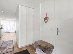 Quarto com um guarda-roupa branco, um banquinho macio e uma decoração em forma de coração na parede.