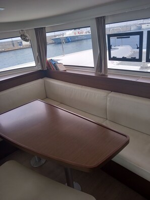 Eine Hütte mit einer gepolsterten Bank und einem kleinen Tisch, ein Fenster mit Blick auf einen Steg und Boote, sowie ein Deckenventilator.