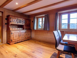 Ein Holzblockhaus-Interieur mit Esstisch, Stühlen und einem Fenster mit Vorhängen.