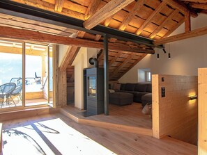 Ein modernes Interieur mit schrägverdeckter Decke, einer integrierten Feuerstelle und einer Sitzecke mit Sofa und Sesseln.