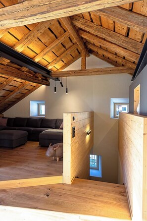 Ein Loft-Zimmer mit schrägem Dach, Holzbalken, einer Couch, einer Schweine-Skulptur und einem kleinen Fenster.