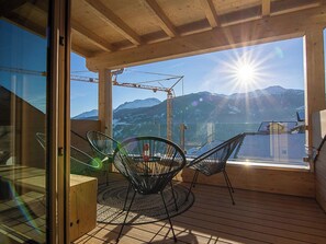 A wooden deck with a glass door leading to a balcony with a view of mountains and a crane in the background. - Ferienhaus Tgioc Ferienhaus, Dusche und Bad, WC, 4 oder mehr Schlafräume by Interhome (Vaz)
