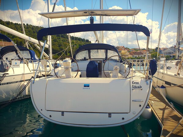 A yacht named 'Ceres Sibinik' docked at a marina with other boats, a clear sky, and a hilly landscape in the background.