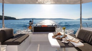 A boat interior with a table, cushions, and a view of the water. - Sun-Kissed Sailing Adventure in Split, Croatia (Kaštel Gomilica)