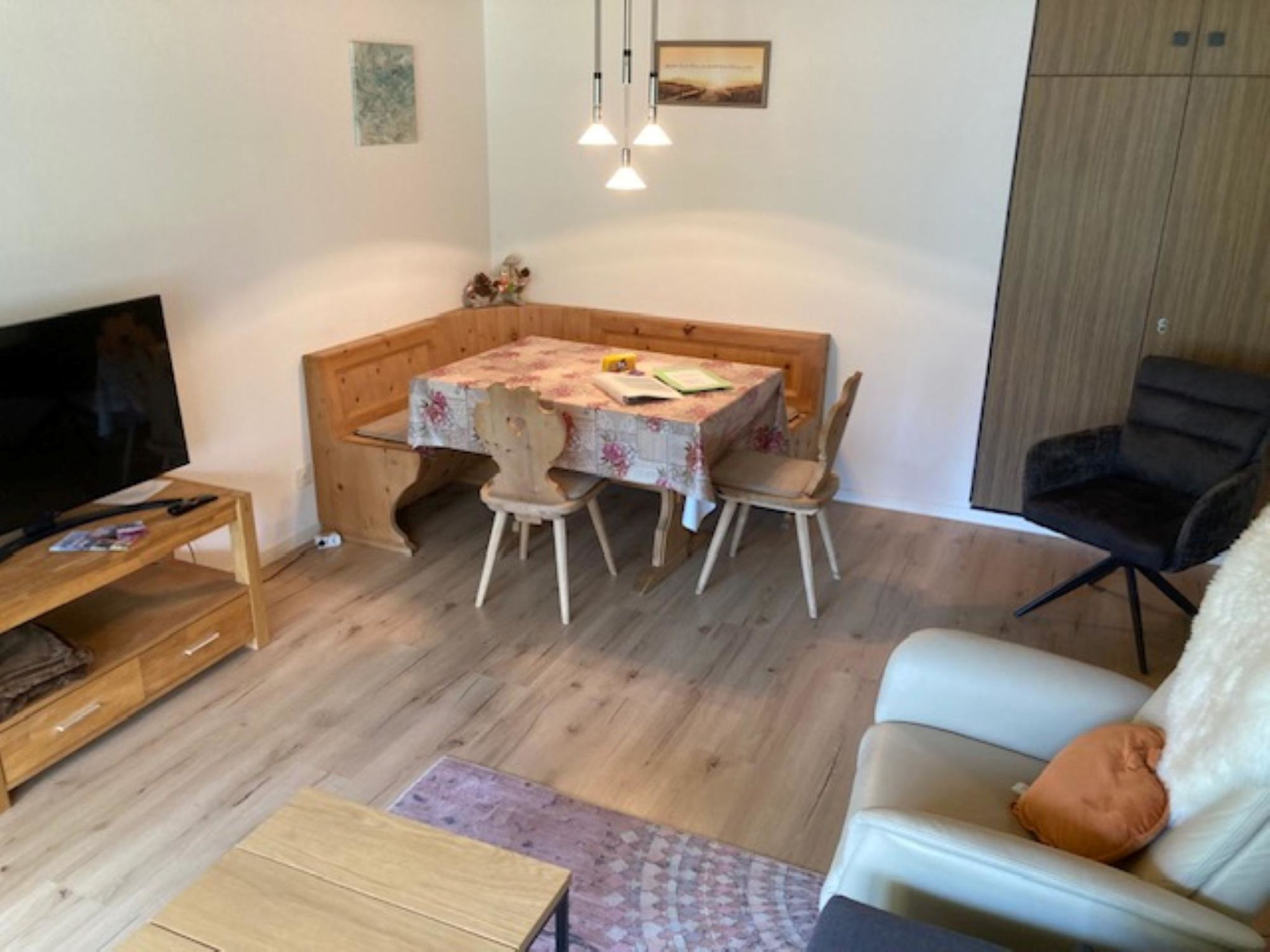 Ein gemütlicher Wohnraum mit Esstisch, Stühlen, einer Couch, einem Fernseher und einem Holzschrank.