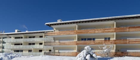 Un immeuble à plusieurs étages doté de balcons, un sol recouvert de neige et un ciel bleu dégagé.