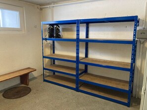 Una estantería metálica azul con tres repisas, un banco de madera y una rejilla en la pared.