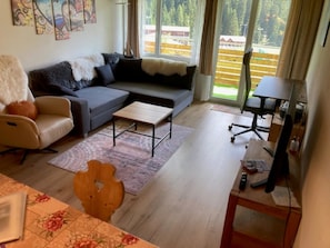 Una sala de estar con sofá, sillón, mesa de centro y escritorio con computadora.