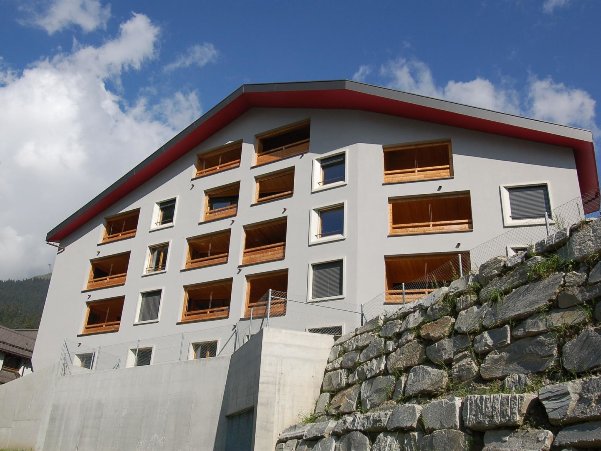 Un edificio de varios pisos con tejado rojo y numerosas ventanas, rodeado por un muro de piedra.