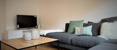 A modern living room with a grey sofa, a flat-screen TV, a wooden coffee table, and decorative vases.