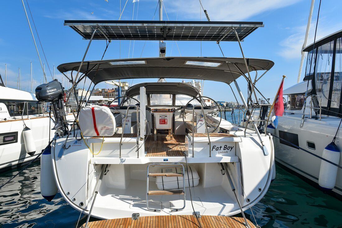 A yacht docked at a marina with a name 'Fat Boy' on the bow, solar panels, and a lifebuoy.