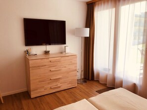 A hotel room with a wooden dresser, a flat-screen TV, a floor lamp, and a bed.
