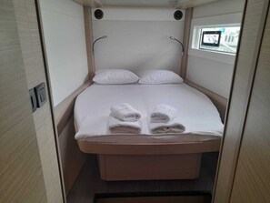 Ein kleines, abgeschlossenes Schlafzimmer mit einem Bett, Kissen und ordentlich gefalteten Handt üchern.