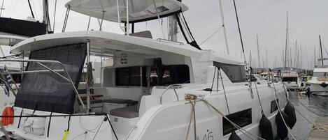 A white yacht docked at a marina with a covered deck area, a seating arrangement, and a number '46' on the side.
