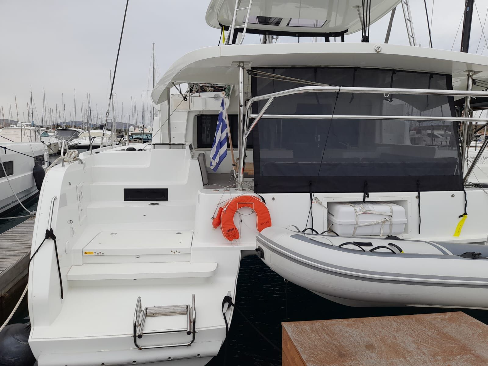 A marina with a white yacht docked, featuring a lifebuoy, a small boat, and a wooden table.