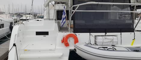 A marina with a white yacht docked, featuring a lifebuoy, a small boat, and a wooden table.