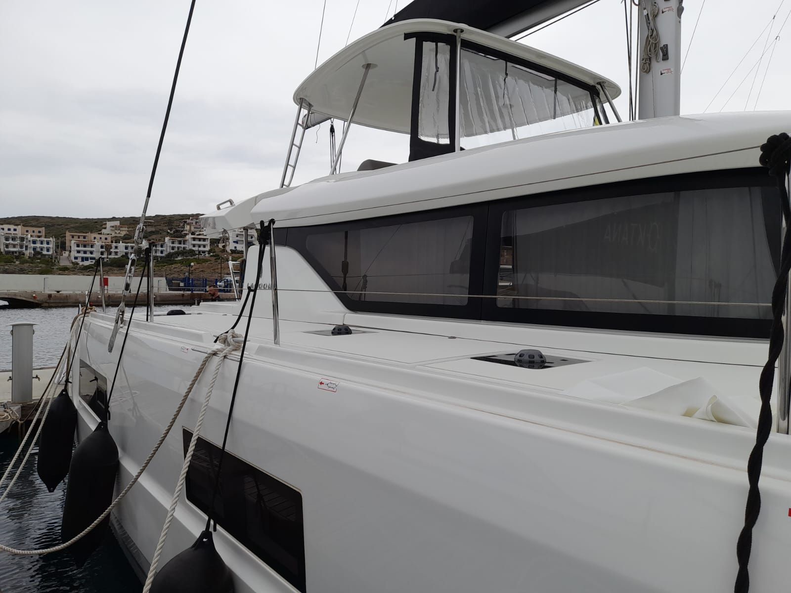 A white yacht docked at a marina with a view of buildings in the background.