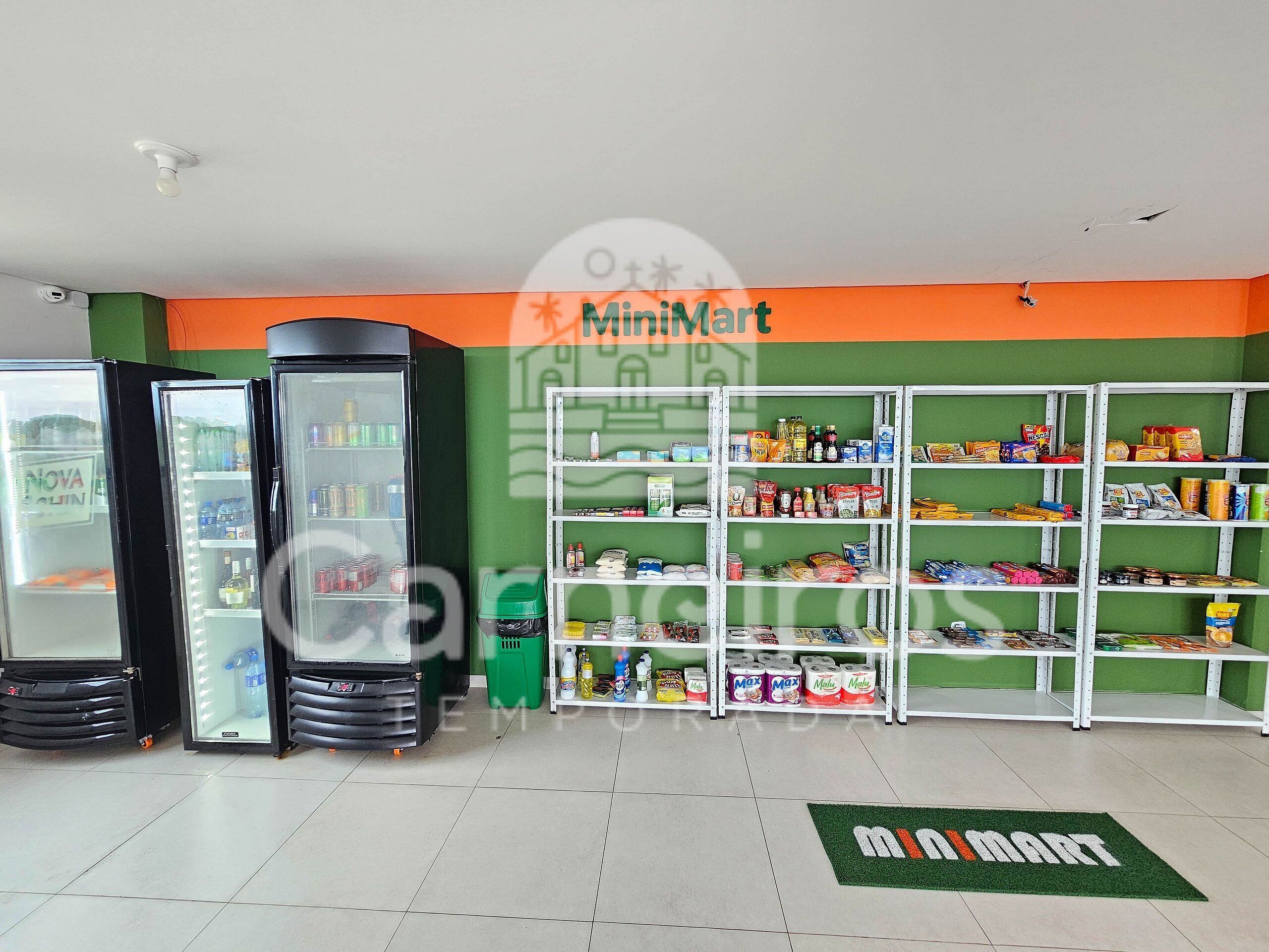 Un MiniMart con vitrinas refrigeradas, estantes repletos de diversos productos y un tapete verde con el logotipo del MiniMart.
