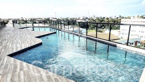 A rooftop swimming pool with a wooden deck and a city view.