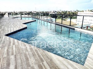 A rooftop swimming pool with a wooden deck and a city view.