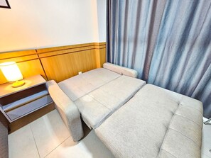 A compact room with a bed, a bedside table with a lamp, and a curtain.