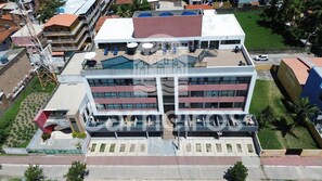 A multi-story hotel with a rooftop terrace, a swimming pool, and a parking area.
