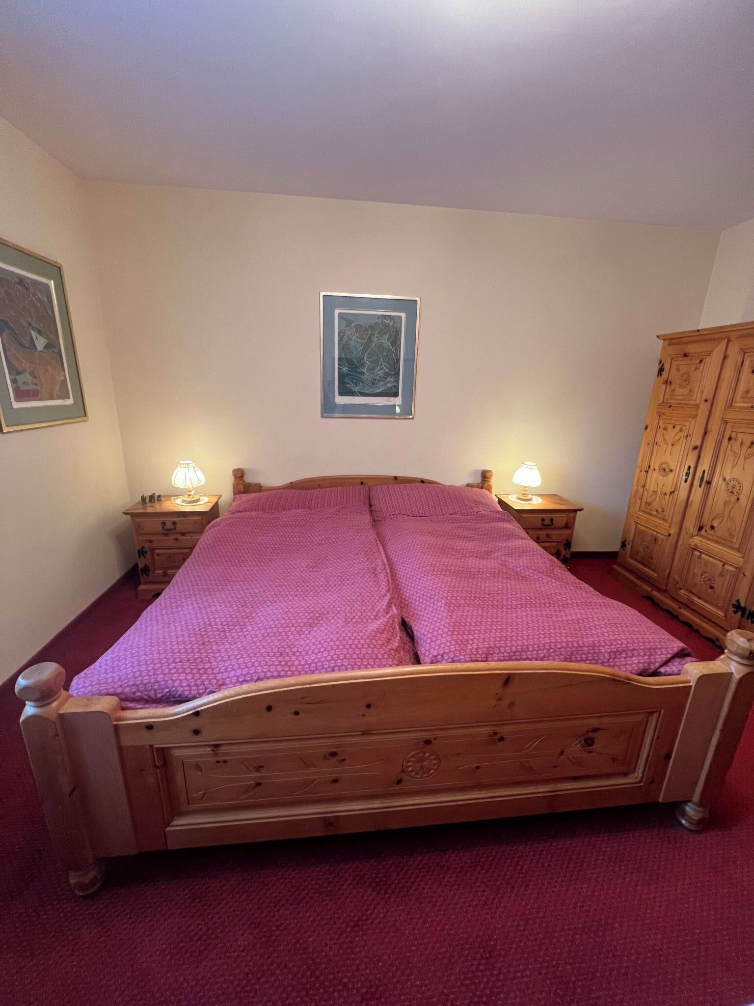 Une chambre à coucher avec un lit en bois, deux tables de chevet avec des lampes, une armoire et un tableau encadré au mur.
