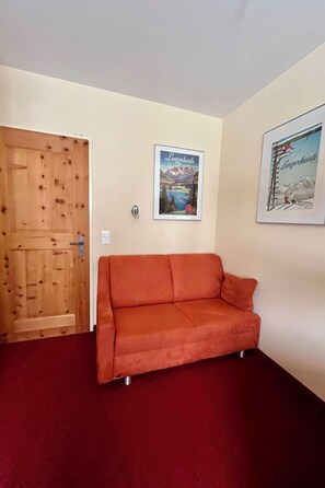 Ein Zimmer mit einer Holztür, einem roten Sofa und zwei gerahmten Bildern an der Wand.