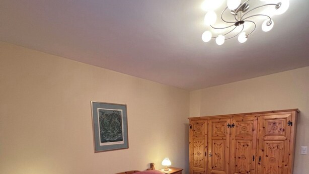 Un dormitorio con cama de madera, una mesita de noche con lámpara, un armario y un candelabro en el techo.