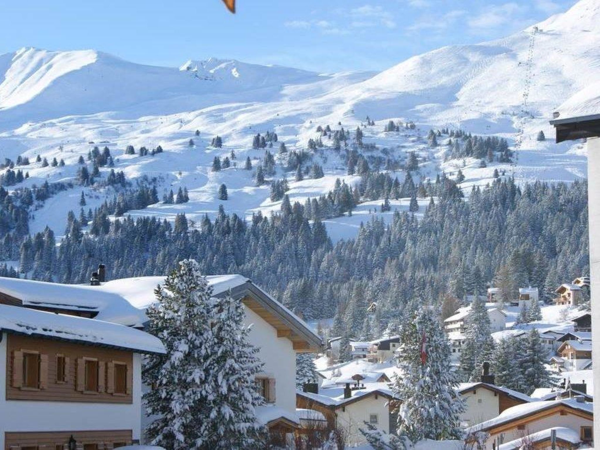 Ein verschneites Bergdorf mit traditionellen Holzhäusern und einer Skipiste im Hintergrund.