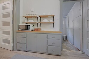 A kitchen with a microwave, wooden shelves, and grey cabinets.