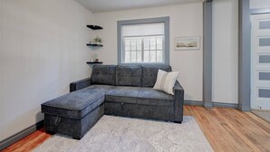 Uma sala de estar moderna com um sofá seccional cinza, uma mesinha lateral, uma janela com persianas e um tapete estampado.