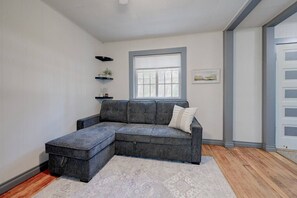 A modern living room with a grey sectional sofa, a small side table, a window with blinds, and a patterned rug. - Quaint cabin at the Lake (Sylvan Lake)
