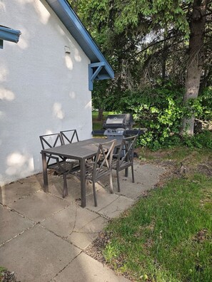 An outdoor patio with a grill, a table, and chairs.