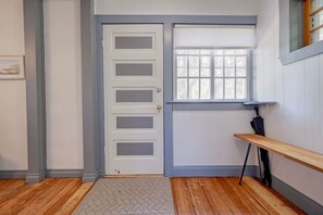 A room with a white door, a window with blinds, a wooden bench, and a door mat. - Quaint cabin at the Lake (Sylvan Lake)